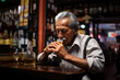Old hispanic man holding a glass of tequila sitting at a bar counter