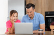 © Pixel-Shot - Happy father and daughter using laptop in kitchen at home
