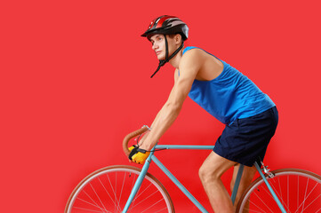 Wall Mural - Young man riding bicycle on red background