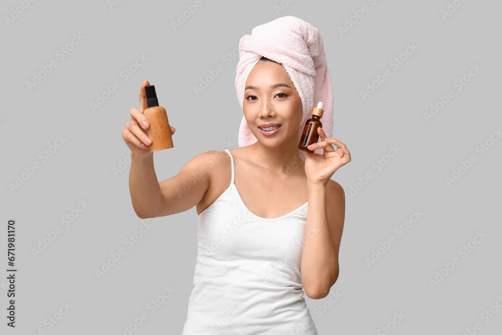 Young Asian woman with cosmetic bottles on light background