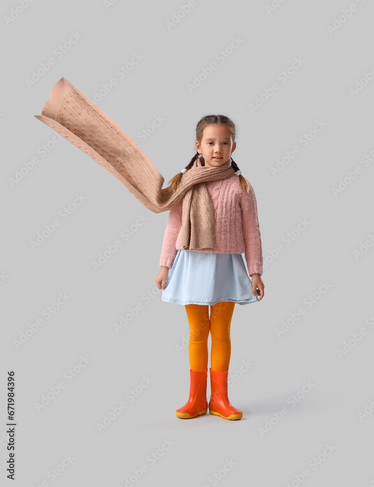 Little Asian girl in rubber boots on light background