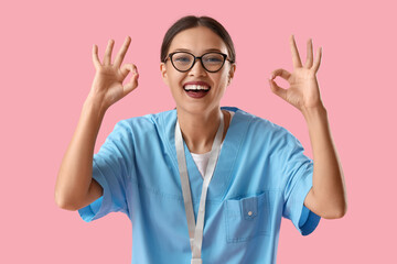 Wall Mural - Asian medical intern showing OK on pink background