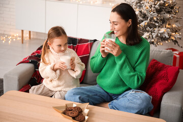 Wall Mural - Happy mother and her little daughter drinking milk with cookies at home on Christmas eve