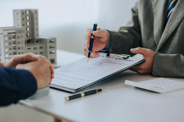 Close-up photo of a real estate agent offering a contract to purchase or rent a residence. Businessman holds small house model with property insurance at table in home sales office