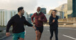 © N Felix/peopleimages.com - Runner group, friends and city on road with talking, progress and happy for fitness, health and wellness. Men, woman and conversation on metro street for workout, training and exercise in Cape Town
