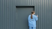 Woman wearing blue coat walks towards the security door and enters her passcode to get in, static