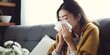 Sick young Asian woman sitting on couch blowing her nose on a tissue conceptual of healthcare, seasonal flu, allergic rhinitis or allergy reaction in hay fever. Closeup, copy space : Generative AI