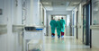 © Wavebreak Media - Diverse male and female surgeons wearing surgical gowns walking in corridor at hospital, copy space