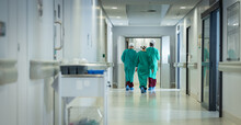 Diverse Male And Female Surgeons Wearing Surgical Gowns Walking In Corridor At Hospital, Copy Space
