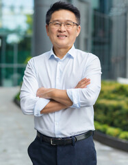 Confident happy mature older business man leader, smiling middle aged senior old professional businessman wearing white shirt glasses crossed arms looking at camera standing outside