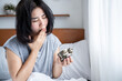 Asian woman wakeup with too much sleepy in morning, yawning and fatigue holding alarm clock in bed