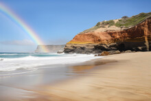 A Beach With Towering Cliffs Of Rainbow-colored Sandstone Rising Up Behind It