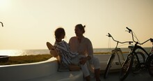 Happy couple in love: a blond guy and a brown-haired girl with a Straw hat who sits on the guy s knee. A guy and a girl are relaxing on their date near the sea where they arrived on their bicycles