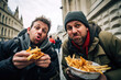Two silly, goofy male friends eating French fries on the street making funny facial expression