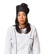 Young Filipina chef with cooking hat in studio shrugs shoulders and open eyes confused.