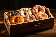 A Wooden Box Holds Assorted Bagels Like Sesame, Plain, And Cinnamon Raisin, Ready For Breakfast