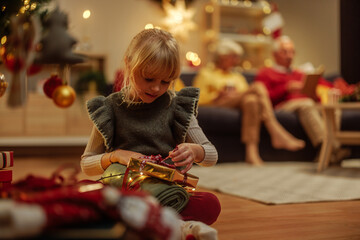 Wall Mural - Happy girl packing Christmas present in front of a Christmas tree