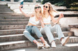 Two young beautiful smiling hipster female in trendy summer white top and jeans clothes. Carefree women posing in the street. Positive models having fun outdoors. Cheerful and happy. Take selfie