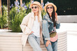 Two young beautiful smiling hipster female in trendy summer clothes. Carefree women posing in the street. Positive models having fun outdoors at sunny day. Cheerful and happy. In hat, sunglasses