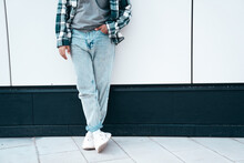Man In Casual Street Style Clothes Posing In The Street. Model In Blue Jeans, Shirt And Sneakers Stands Near Wall. Unrecognised, No Face