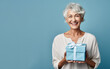Beautiful mature woman 50, 60, 70 years old on a blue background holding a large gift box, holiday surprise, compliment bonus for birthday anniversary