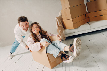 Happy young family couple man haul move woman inside box. Moving with cardboard boxes to new home apartment concept