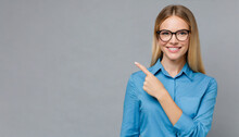Happy Young Smiling Professional Business Woman Wearing Blue Shirt Looking At Camera Pointing Finger Away At Copy Space Showing Aside Presenting Advertising Offer Standing Isolated At Gray Background
