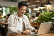Young Asian man sitting in a cafe working at his laptop. Freelance distant work business management concept