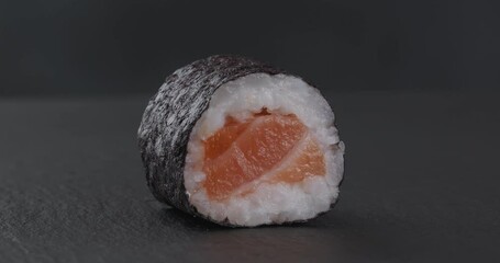 Wall Mural - Traditional Japanese maki roll with salmon on a dark background. Close-up footage on the rotating table.