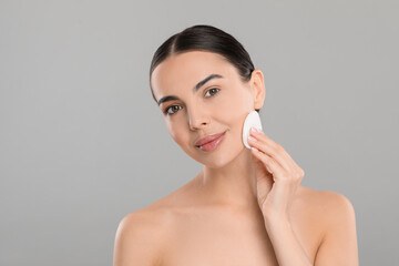 Wall Mural - Beautiful woman removing makeup with cotton pad on light grey background, space for text