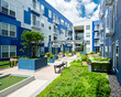 A nice modern apartment building outdoor amenity space with seating, landscaping, and gardens. The building is blue and white. the sky is partly cloudy