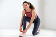 © brizmaker - Smiling woman in sportswear exercising in the gym, lacing up her shoes.