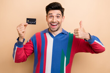 Sticker - Photo of astonished man hold plastic debit card demonstrate thumb up approval isolated on beige color background