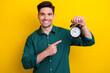 Photo of cheerful satisfied man wear green stylish clothes showing alarm clock isolated on yellow color background