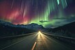 Photo of mountains during the northern lights, long straight asphalt road with light at the end of the route.