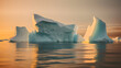 Icebergs drift calmly in a cold, still ocean, in the warm light of a cloudless sky. The ice's pristine reflection graces the water, creating a serene spectacle.