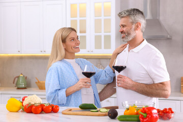 Wall Mural - Happy affectionate couple with glasses of wine cooking together at white table in kitchen