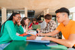 © Jose Calsina - Happy multiracial group of high school students working together, sitting at library with notebooks, writing and using a laptop to search information. Young teenagers studying exams at university