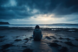 Fototapeta Morze - Distressed individual sitting alone displaying sadness on an eerily quiet beach 