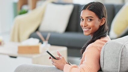 Canvas Print - Portrait of a woman texting and browsing online social media on a phone while relaxing on the couch at home. One young, smiling and happy Indian girl searching the internet and scrolling on the web