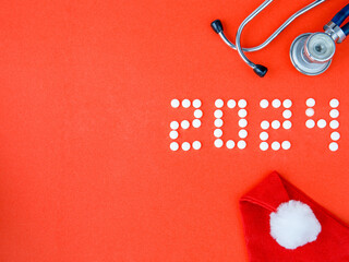 2024 Happy New Year banner for health care and medical concept. Number 2024 made from tablets, stethoscope and Santa hat on a red background. View from above flat lay. Medical concept. Copy space