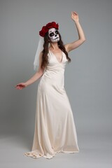 Wall Mural - Young woman in scary bride costume with sugar skull makeup and flower crown posing on light grey background. Halloween celebration