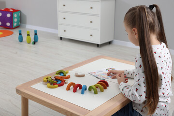 Wall Mural - Motor skills development. Girl playing with colorful wooden arcs at white table in kindergarten