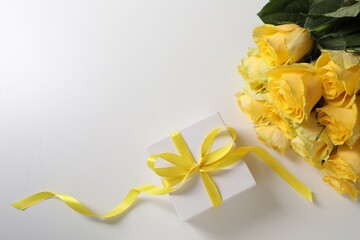 Wall Mural - Beautiful bouquet of yellow roses and gift box on white background, flat lay. Space for text