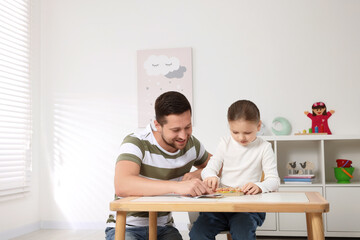 Wall Mural - Motor skills development. Father helping his daughter to play with geoboard and rubber bands at white table in room