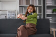 © wichayada - Asian woman listening to music while sitting on the sofa Attractive young woman wearing headphones feels happy spending free time at home and enjoying weekend activities at home.