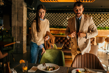 Wall Mural - Two coworkers, a man, and a woman, taking off their jackets, picking their lunch at a restaurant