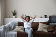 © fizkes - Happy young African American woman relaxing on sofa at home, resting on couch, breathing cool fresh conditioning air, enjoying leisure time in ventilated living room. Comfortable house concept