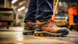 © PaulShlykov - Close-up safety working shoe on a worker feet is standing at the factory, ready for working in danger workplace concept. Industrial working scene and safety equipment.