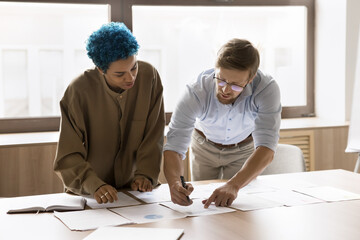 Busy young colleagues, business partners working on marketing strategy together, discussing paper statistic reports, studying documents on table, talking, brainstorming